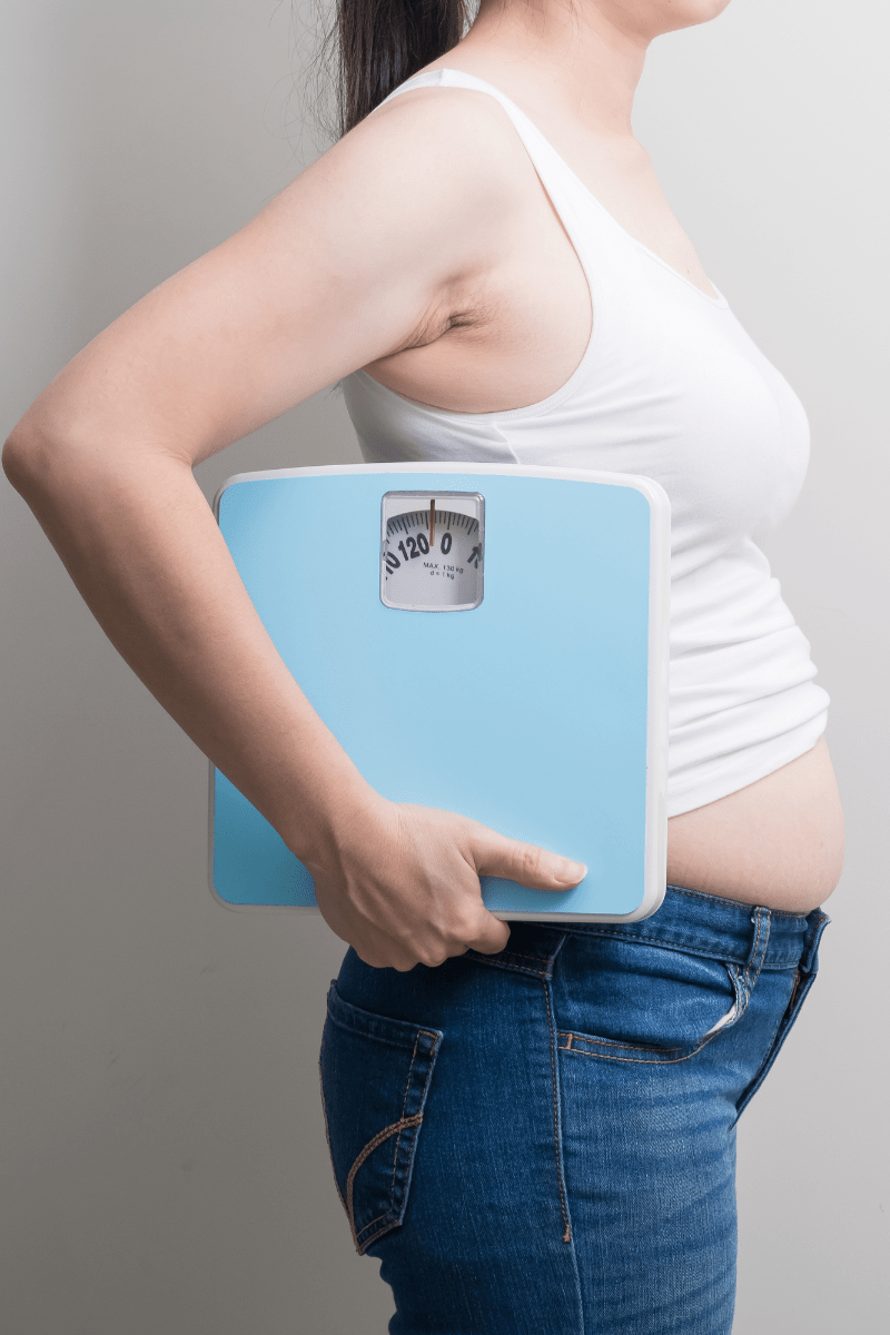 a bloated middle aged woman holding a set of weighing scales.